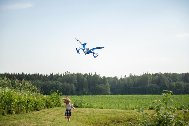 Rear view of happy child girl with a kite blue butterfly running on meadow in summer nature