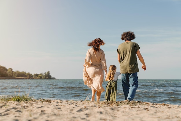 Rear view of happy family walking and having fun on the beach with cute little girl