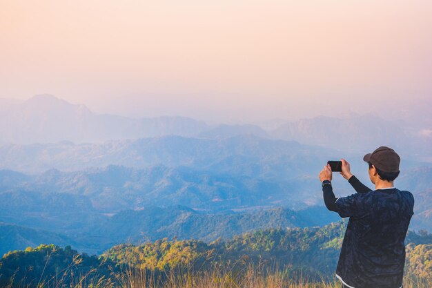 Rear view of hiker person photographing against sky on top mountain