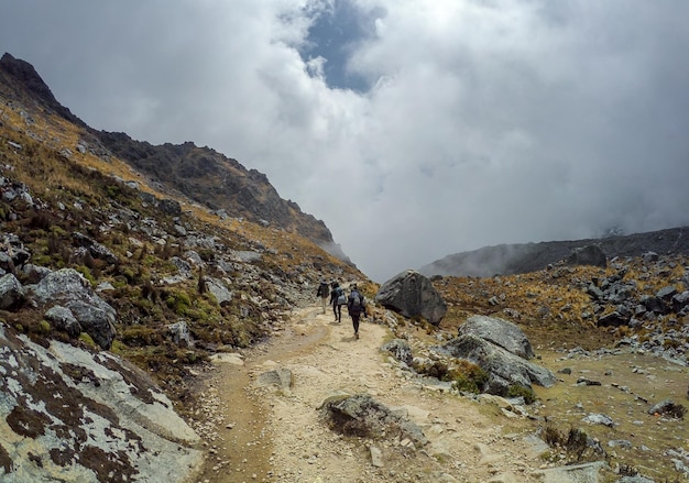 雲の空を背景に山を歩くハイカーの後ろの景色