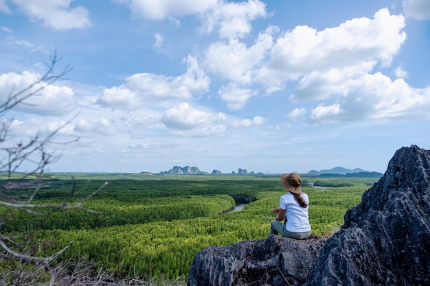 Rear view image of a beautiful young asian woman sitting on the mountain peak while traveling the mangrove forest viewpoint