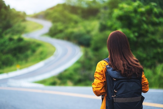 Photo rear view image of a female traveler with backpack walking along a mountain road