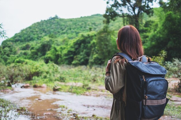 Rear view image of a female traveler with backpack walking by mountain stream for hiking concept