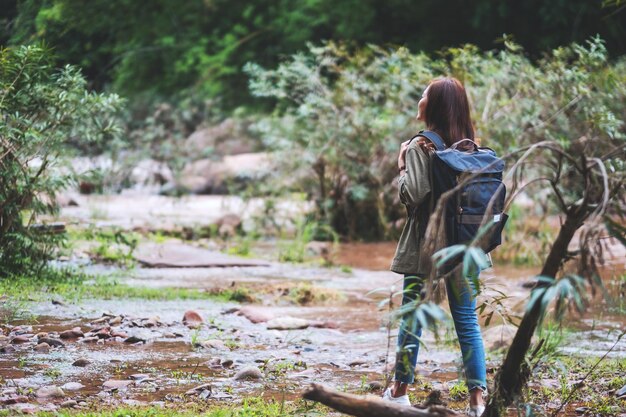 Rear view image of a female traveler with backpack walking by mountain stream for hiking concept