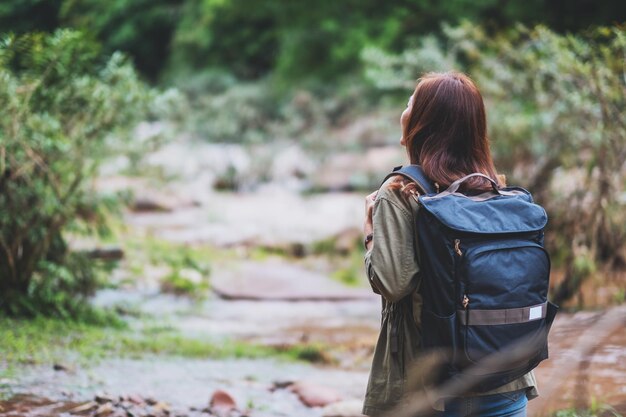 Rear view image of a female traveler with backpack walking by mountain stream for hiking concept