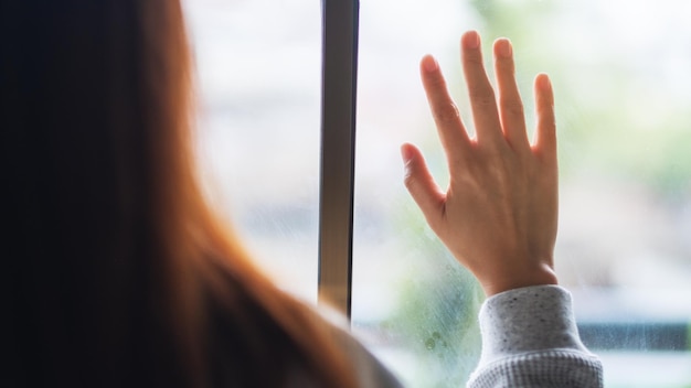 Photo rear view image of a sad woman touching on window while looking outside