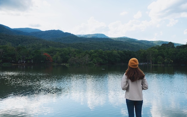 湖のほとりの美しい緑豊かな山々を見ている女性の背面図