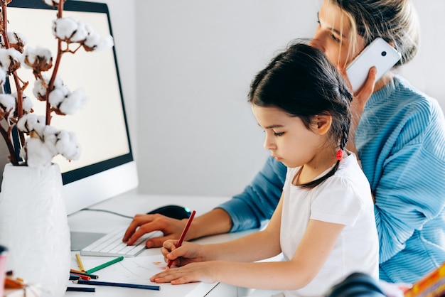 Foto immagine vista posteriore di una giovane donna con la figlia seduta a casa e al lavoro giovane madre con un bambino che lavora al computer e gioca madre casalinga seduta con il suo bambino e al lavoro