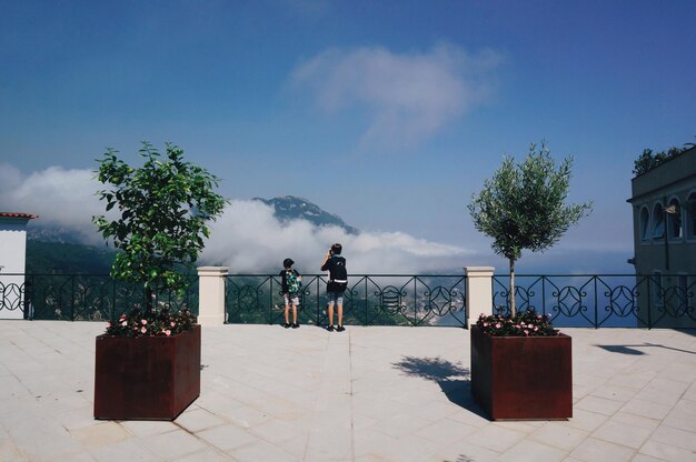 Vista posteriore di bambini in piedi accanto alla ringhiera che guardano la montagna contro il cielo