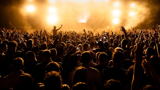 Photo rear view of large group of people having fun at music concert while watching live performance on the stage