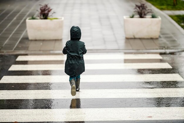 雨天の通りを横切って歩いている少年の後姿