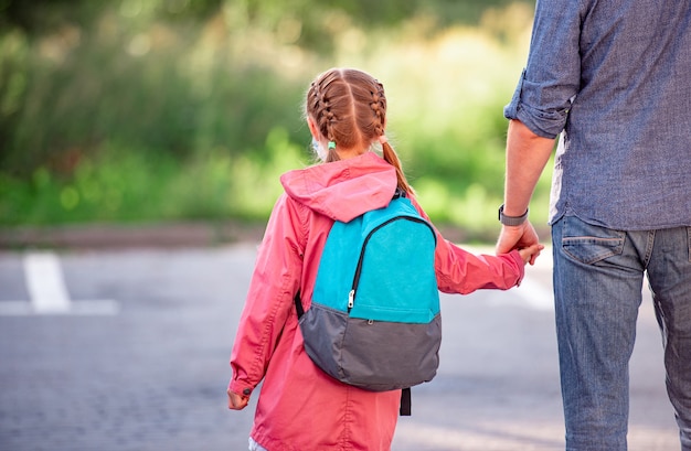 Вид сзади маленькой девочки с рюкзаком, держащей руку отца