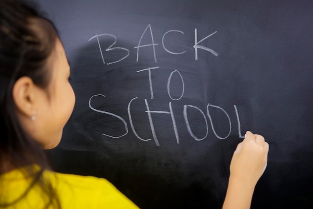 Вид сзади на маленькую девочку, пишущую текст "обратно в школу"