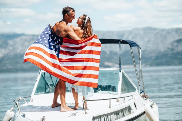 Rear view of a loving couple with us national flag having fun\
and spending the day on her private yacht.