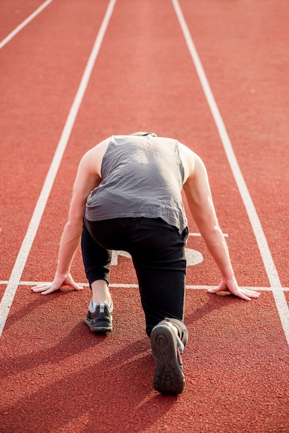 Foto retrovisione di un atleta maschio che prende posizione sulla pista di corsa rossa per correre