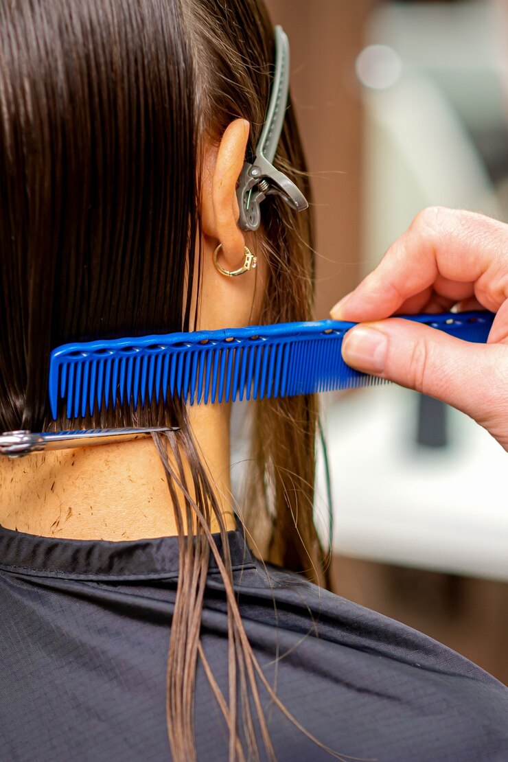 Rear view of a male hairdresser cuts hair of young woman with siscors and comb