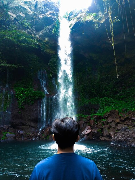 Foto vista posteriore dell'uomo contro una cascata nella foresta