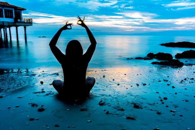 Foto vista posteriore di un uomo che fa yoga sulla spiaggia durante l'alba