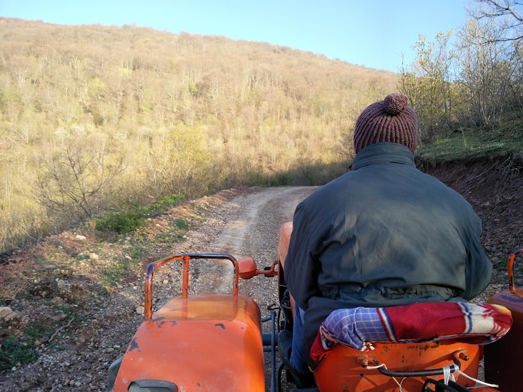 Photo rear view of man driving tractor on dirt road against mountain