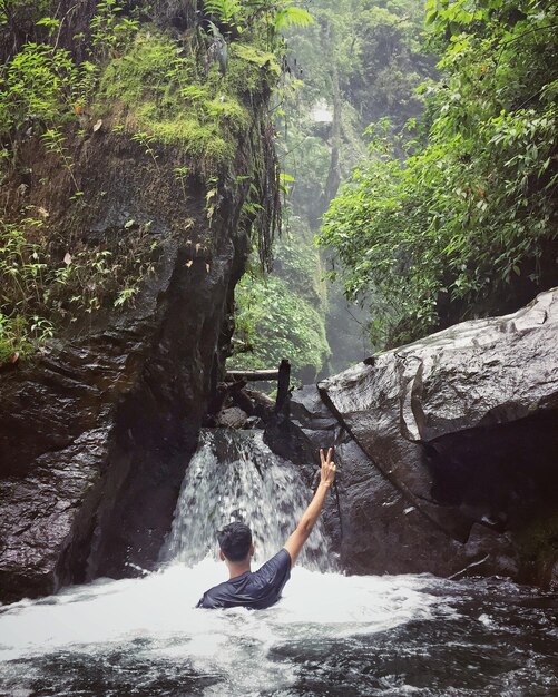 Foto vista posteriore di un uomo che si diverte in una cascata tra le rocce della foresta