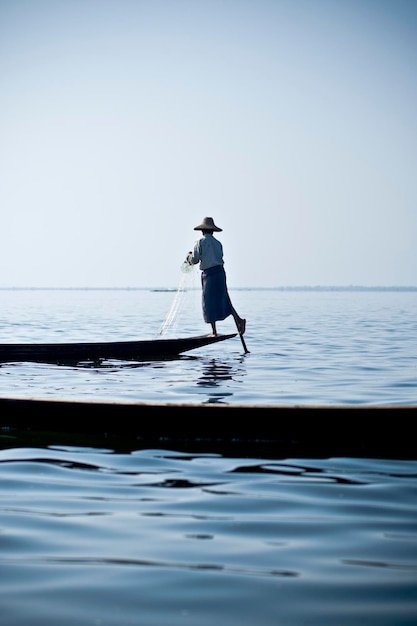 rear view of man fishing on boat against blue sky