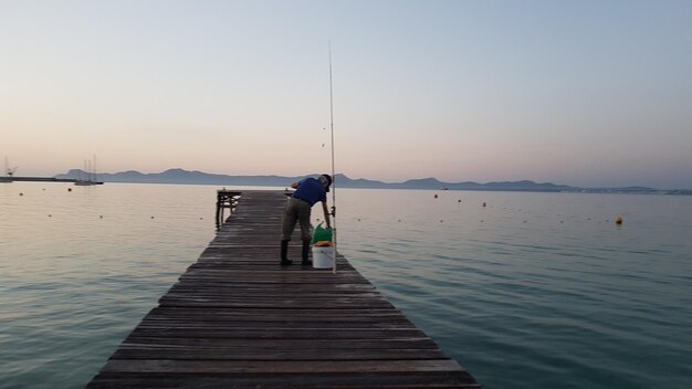 Rear view of man fishing on pier at lake