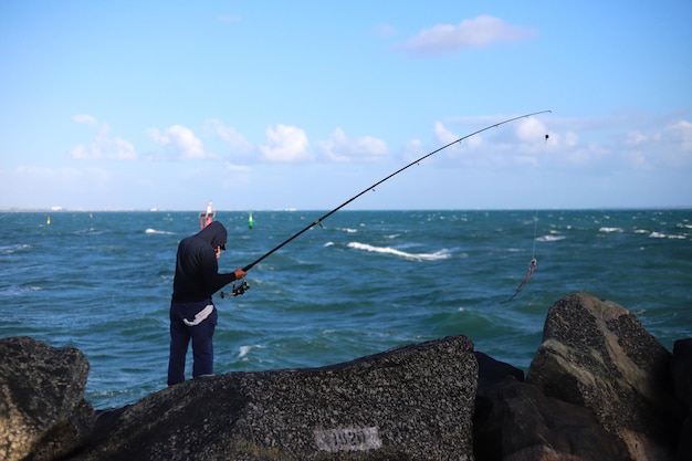 Rear view of man fishing in sea against sky