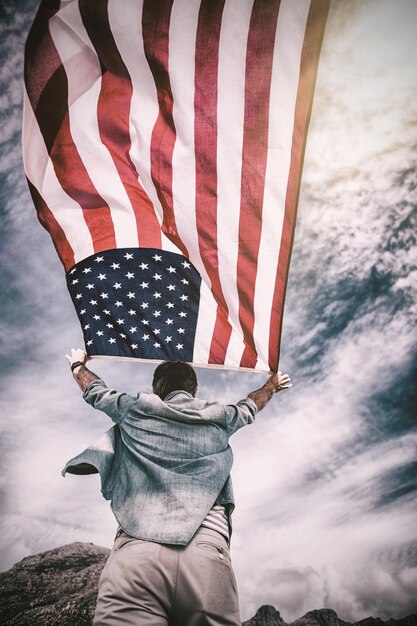 Rear view of man holding american flag against sky