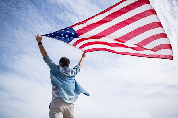 Rear view of man holding american flag on beach