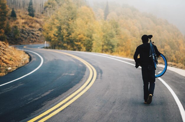 Foto vista posteriore di un uomo che tiene in mano una bicicletta sulla strada