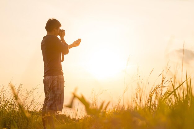 Rear view of man holding camera while standing on land against sky during sunset