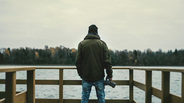 Photo rear view of man holding camera while standing on pier