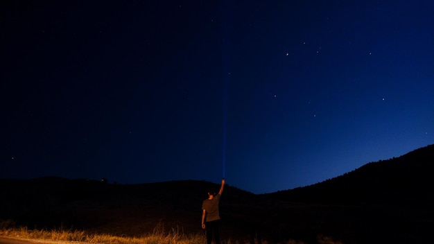 Photo rear view of man holding illuminated flashlight against sky at night