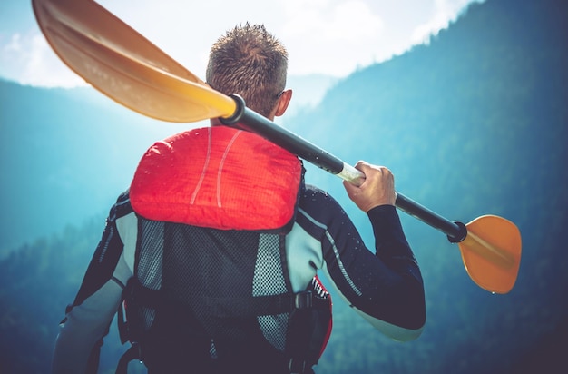 Photo rear view of man holding oar against mountains