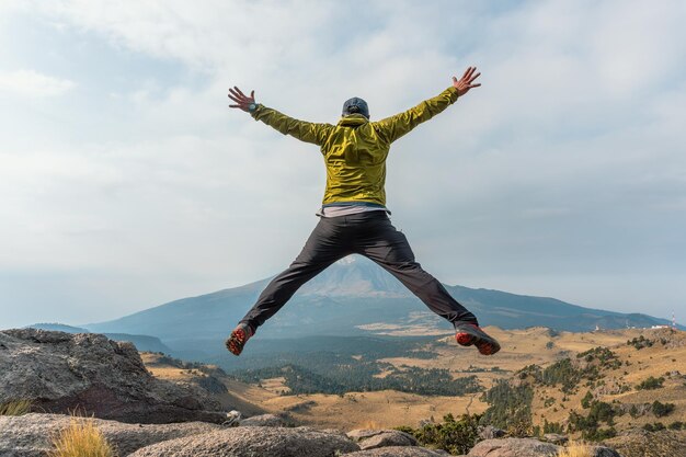 Foto vista posteriore di un uomo che salta su una scogliera contro il paesaggio