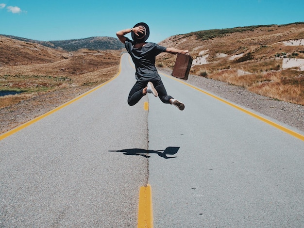 Foto vista posteriore di un uomo che salta su una strada di campagna contro il cielo