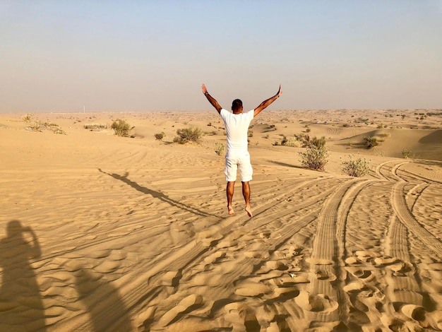 Rear view of man jumping with arms raised on sand at desert