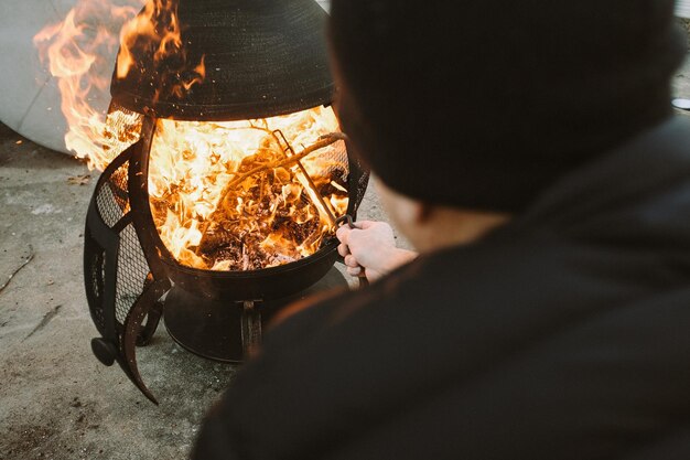 Foto vista posteriore di un uomo che accende il fuoco in un contenitore nel cortile sul retro