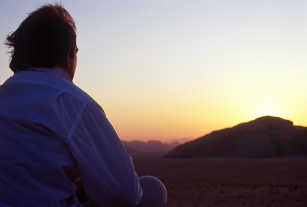 Rear view of man looking at mountains against sky during sunset