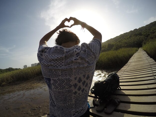 Foto vista posteriore di un uomo che fa la forma di un cuore sulla passerella contro il cielo