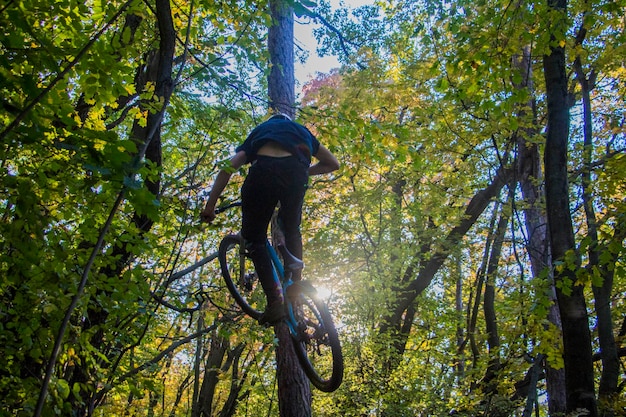 Foto vista posteriore di un uomo in aria che fa uno stunt con una bicicletta in foresta