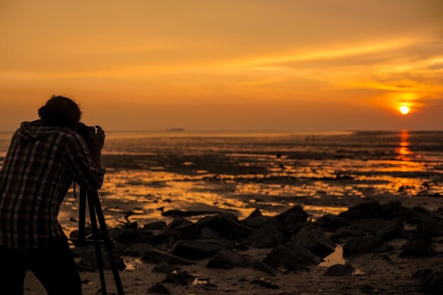 Photo rear view of man photographing sea during sunset