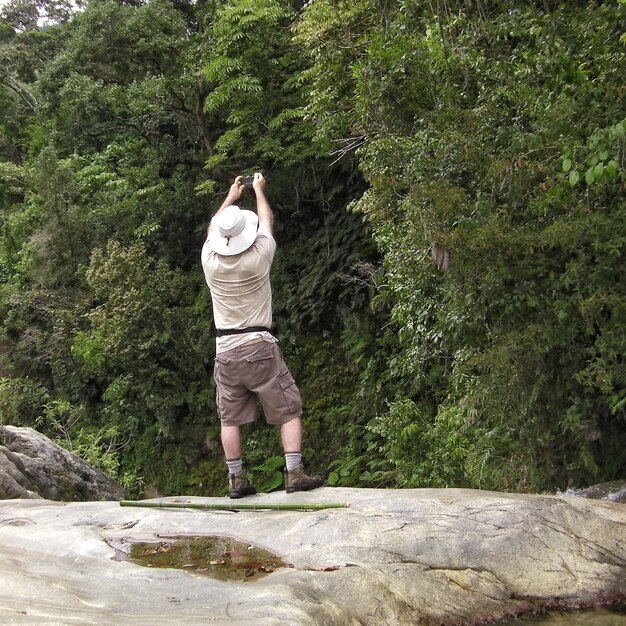 Rear view of man photographing trees while standing on rock