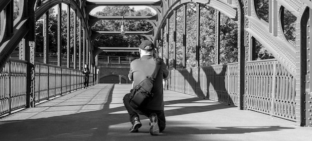 Foto vista posteriore di un uomo che scatta fotografie mentre è in ginocchio su un ponte pedonale