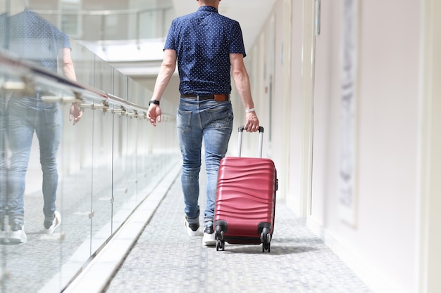 Rear view of man pulling suitcase down hotel corridor