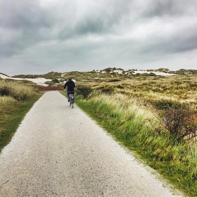 Photo rear view of man riding bicycle on road leading towards cloudy sky