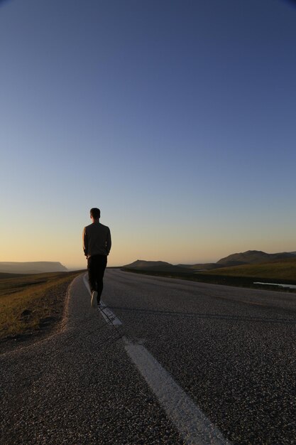 晴れた空を背景に道路を歩く男の後ろの景色