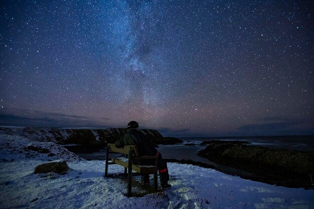 夜の空に向かってベンチに座っている男の後ろの景色