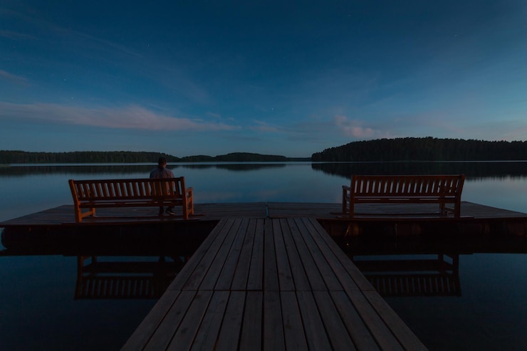 Photo rear view of man sitting on bench on pier over lake against blue sky at dusk