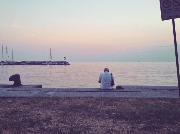 Photo rear view of man sitting by sea against clear sky